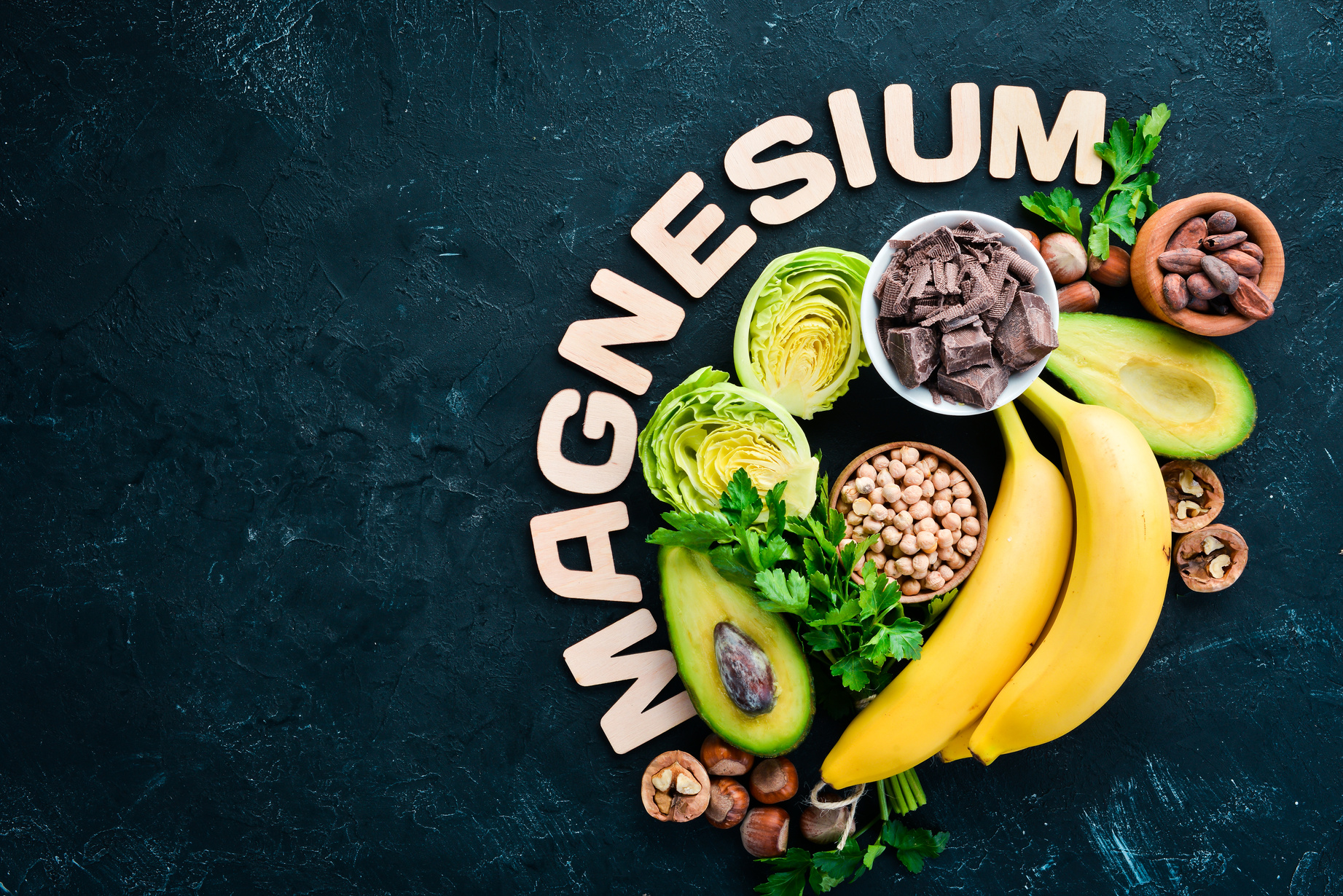 Foods containing natural magnesium. Mg: Chocolate, banana, cocoa, nuts, avocados, broccoli, almonds. Top view. On a black background.